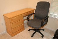 Photo showing the wooden desk with four drawers next to the gray fabric office chair in a corner near a window.