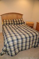 Full bed view with plaid bedding and wood headboard in a room.