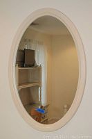 Oval mirror mounted on wall reflecting a room with a bookshelf, chair, and TV.