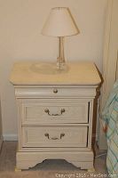 Beige Lexington Furniture nightstand with three drawers and metal handles, lamp on top