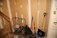 Two 36-inch wrought iron hanging plant stands with hanging pots, positioned near stairs, along with garden tools including rake, broom, shovel, and pruner.