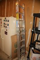 Aluminum ladder folded and leaning against a wall near a fridge in a garage.