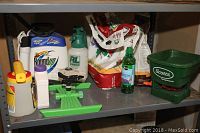 Photo shows a variety of gardening chemical containers, plant food bags, a handheld Scotts spreader, and spray bottles on a metal shelf.