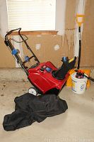 Full view of Toro snowblower with black cover, yellow snow shovel and white bucket nearby.