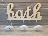 Front view of wooden “bath” sign with three hooks