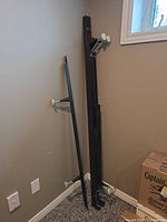 Folded black metal queen bed frame with center support and glide feet leaning against wall