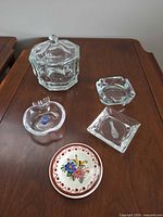 All five items displayed: glass candy dish with lid, two ashtrays, apple-shaped dish, ceramic dish