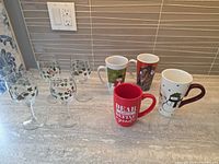 Group shot of four wine glasses and five Christmas mugs on countertop