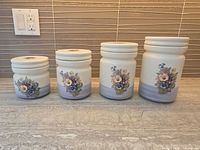 Front view showing four graduated floral stoneware canisters