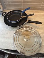 Three frying pans nested together with stainless steel universal lid