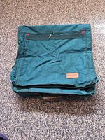 Folded garment bag front showing zip pocket and logo patch