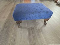 Top and legs of navy floral upholstered foot stool on wood floor