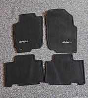 Four black Toyota RAV4 carpet floor mats laid out on carpeted surface showing topside logos and shapes