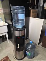 Water cooler with one jug mounted on top and second jug on floor