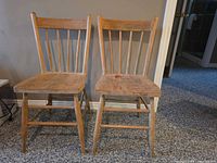 Front view of two stripped wooden spindle-back chairs showing missing side rungs