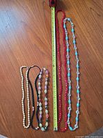 All five necklaces laid out beside tape for length reference