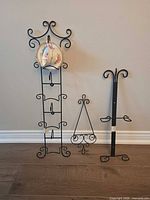 Three black wrought iron display stands and floral teacup on tall rack