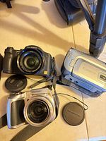 Top view showing Lumix camera, Olympus camera, Canon camcorder and lens caps