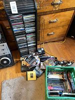 Wide view of CD tower, pile of cassettes, green crate with media, partial DJ unit