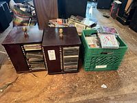 Two wood CD organizers next to green crate filled with numerous CDs on floor