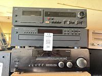 Stack of three audio components showing NAD cassette deck on top, NAD CD player in middle, Kenwood receiver bottom