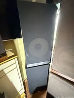 Front view of tall black JBL speaker beside furniture