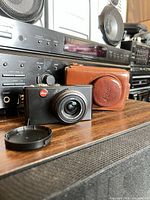 Front view of Leica D-LUX 3 camera, leather case, and lens cap