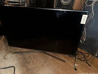 Front view of Samsung flat panel TV on floor with stand and power cord visible