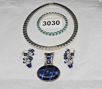 All four jewelry items arranged: collar necklace, stretch bracelet, dangle earrings pair, cabochon pendant