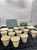 Group view of 11 tea cups, 16 saucers, picture frame, and Lenox box displayed on black quilted surface