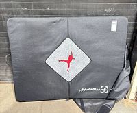 Front of crash pad showing black cover, grey diamond patch with red climber graphic