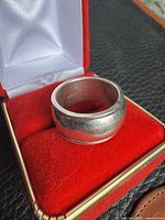 Front view of sterling silver wide-band spinning ring in red presentation box