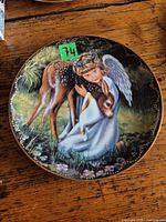 Front view of porcelain collector plate showing angel hugging fawn, gold rim visible