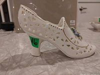 Side profile of porcelain shoe showing heart cutouts, floral appliqué and gold accents