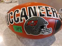 Side view showing BUCCANEERS text and helmet logo on red plush football