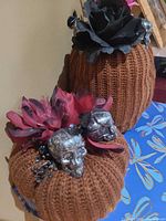 Two brown knit pumpkins with flower and skull decorations placed on a blue surface