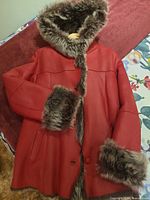 Front view of red lambskin coat showing hood, buttons, pockets and faux fur trim