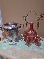 Overall view of silver pot with spoons and pink glass decanter on stand