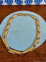 Full view of gold plated Christian Dior choker necklace on blue background