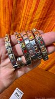 Five stainless steel charm bracelets fanned in hand