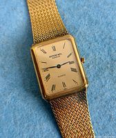 Front view of rectangular watch on blue felt showing dial and bracelet