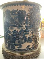 Full view of cylindrical blue and white ceramic jardinière with brass mounts