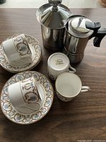 Group showing two cups on saucers, two additional saucers, stainless espresso pot and stainless jug