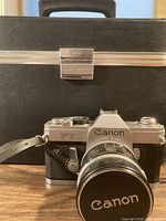 Canon FT QL camera with lens and front cap in front of black hard camera case