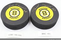 Both signed Boston Bruins pucks showing signatures and team logos