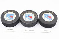 Front view of three signed New York Rangers pucks showing player autographs and logo decals