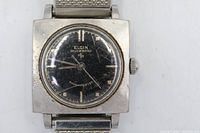 Front view of Elgin Shockmaster watch showing square case, black dial, stretch bracelet, visible scratches on crystal