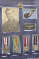 close view of framed contents: portrait, two cloth badges, cap badge and four medals