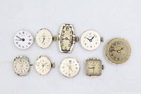 Front view of nine watch movements with dials and crowns