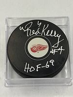 Signed side of puck showing Red Kelly autograph, HOF-69 inscription, number 4, Detroit Red Wings logo, acrylic cube
